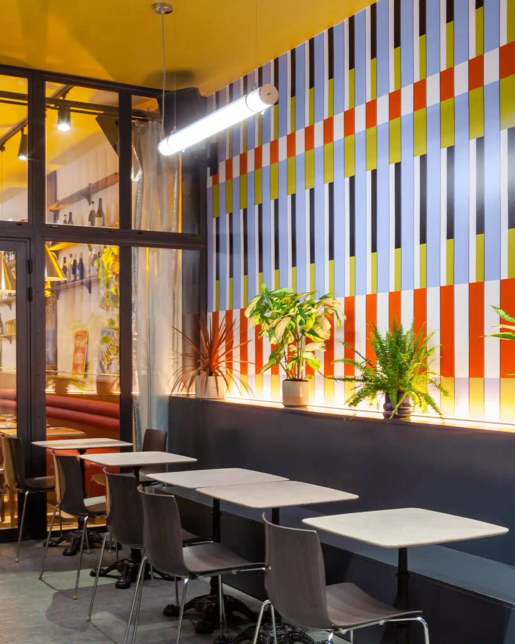 Vue de la salle extérieure du restaurant avec tables en bois et motifs muraux graphiques.